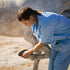 Vet in blue checks horse's hoof outside.